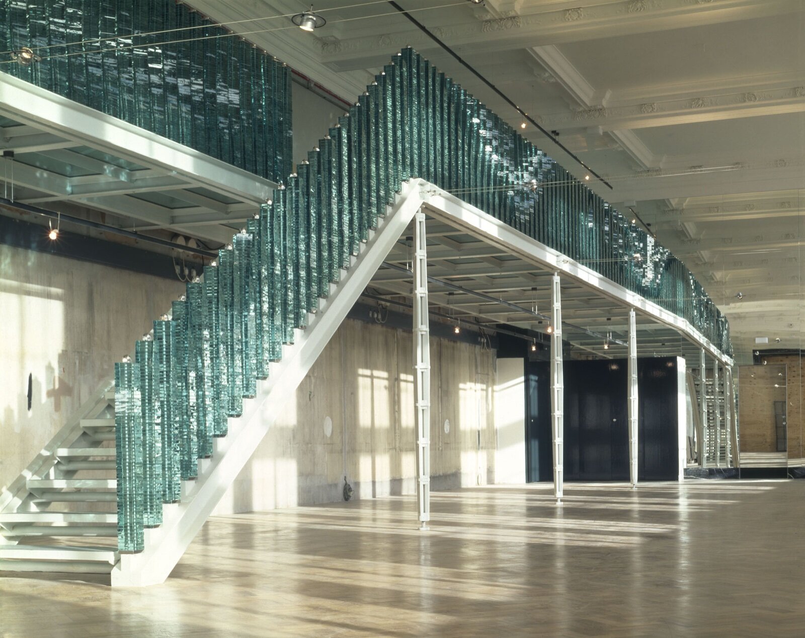 A stacked glass balustrade running up an open-tread stair and along the edge of a gallery floor