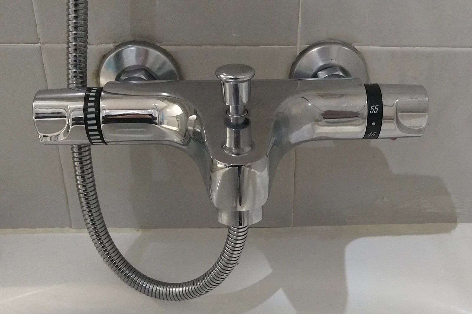Chrome thermostatic bath and shower mixer on a tiled wall above a bath