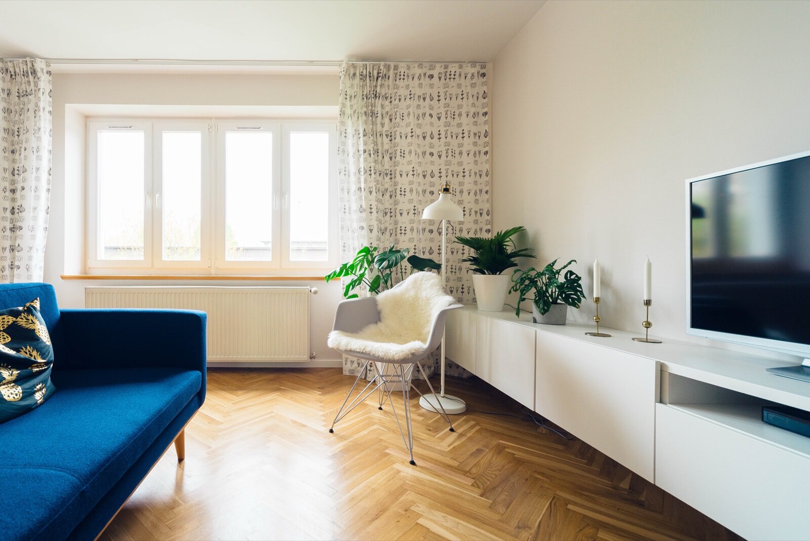 A bright, modern living room with a blue sofa, a midcentury chair and a herringbone wood floor