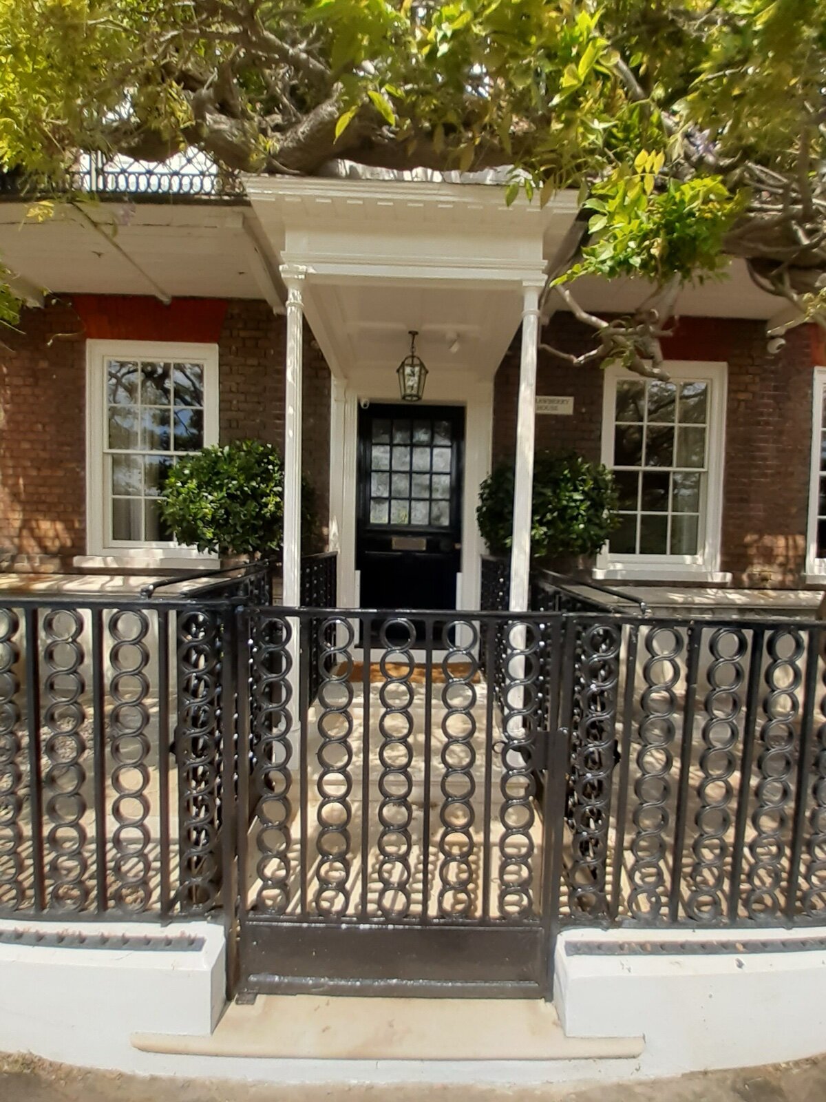A white timber open porch with slender columns over the black front door of a Georgian brick house, behind black railings