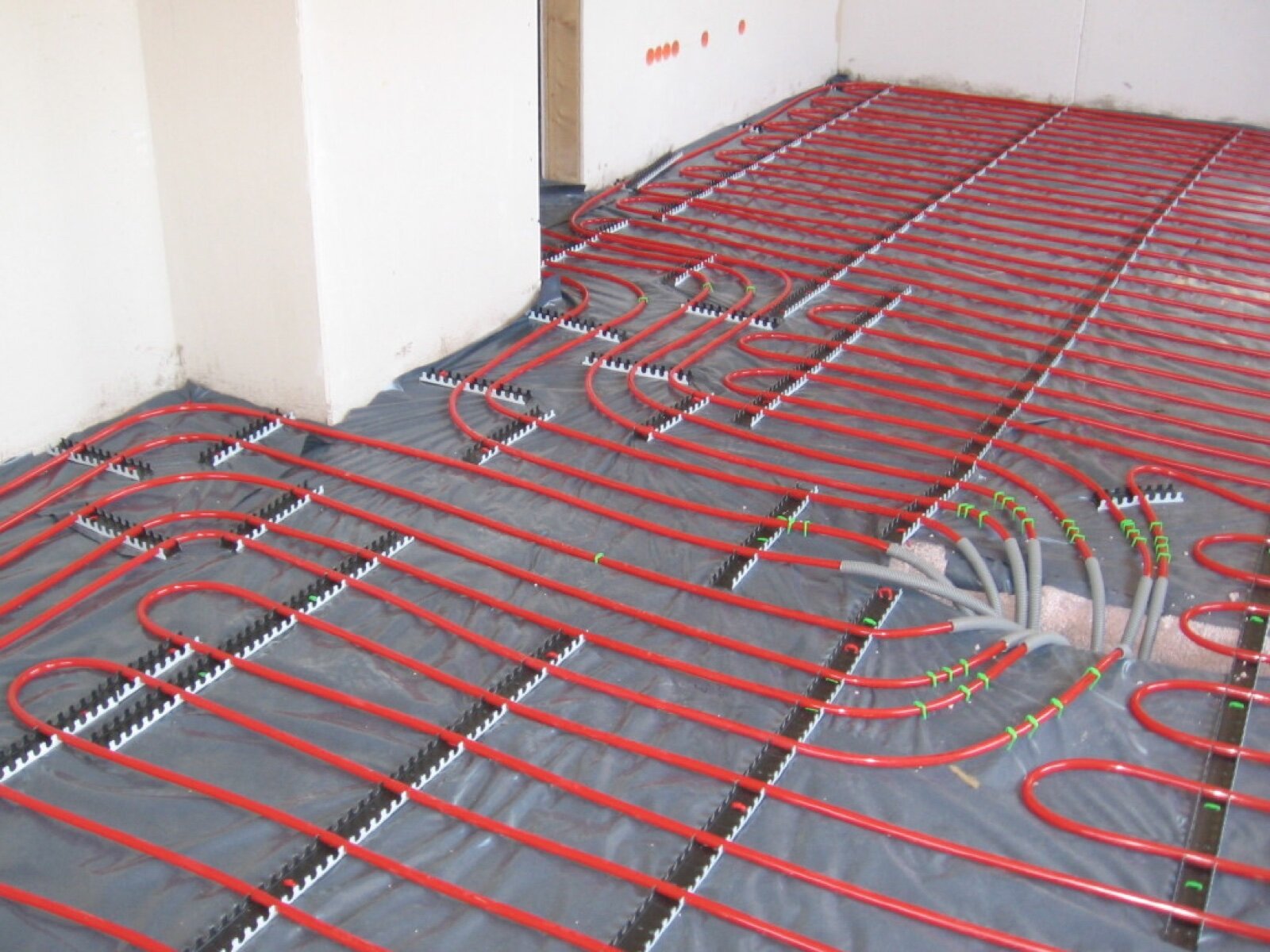 Red underfloor heating pipes clipped in rows to a membrane over insulation, ready for screed
