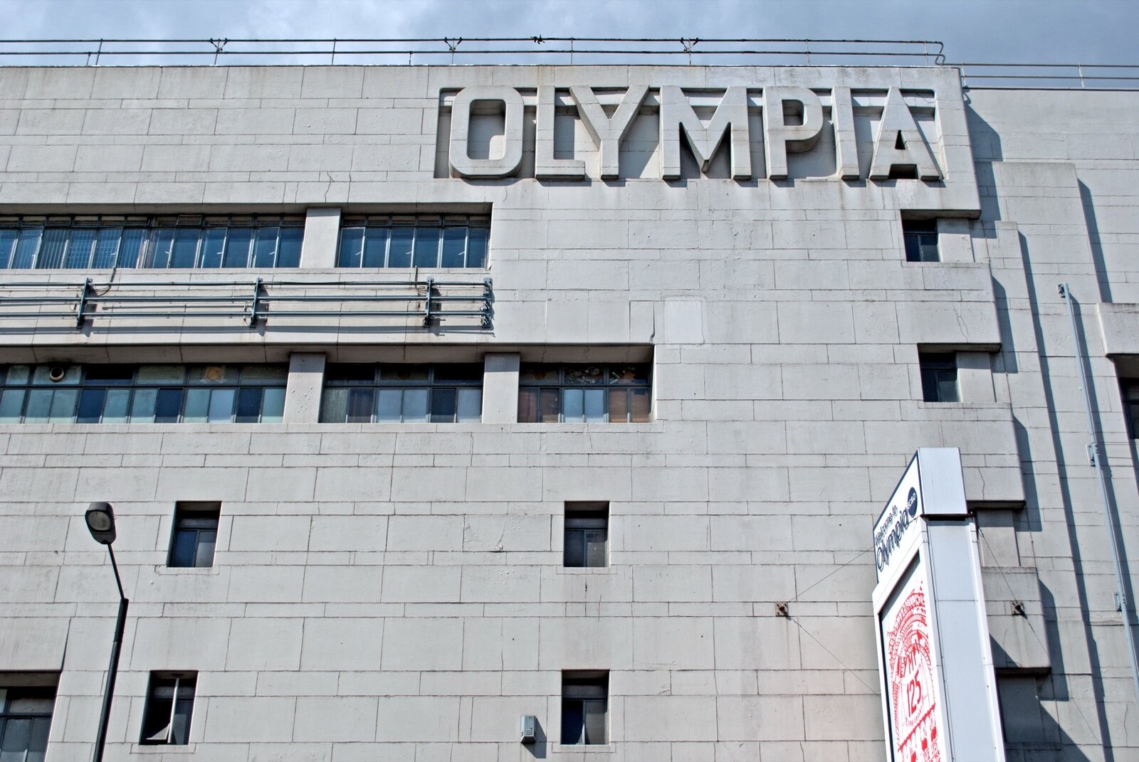The stone facade of Olympia exhibition centre in west London with OLYMPIA in large raised letters near the roofline